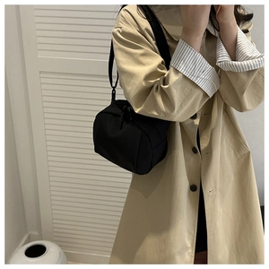 Close-up of a minimalist black nylon crossbody bag worn with a beige trench coat
