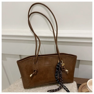Détail du cabas en similicuir marron avec logo embossé et breloque tissée élégante