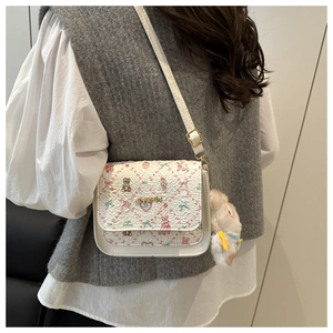 White crossbody bag with bear print and plush charm shown on person in soft indoor lighting