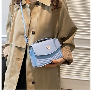 Close-up of light blue quilted crossbody bag with golden butterfly buckle detail