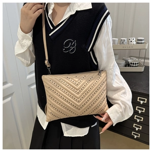 Detail of apricot quilted crossbody bag with stud accents worn by a female model