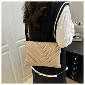 Beige quilted envelope bag with rivets shown worn cross-body on model back view