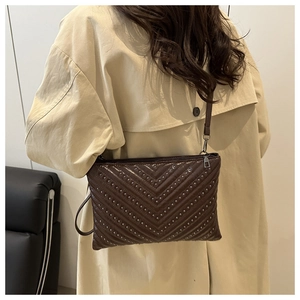 Detail of dark brown crossbody bag with V-shaped quilting and metal studs on leather surface