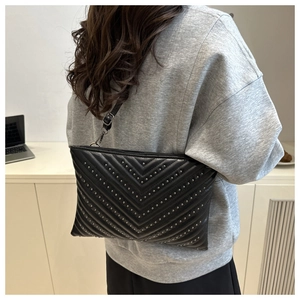 Detail of black quilted leather envelope bag with silver studs and adjustable strap