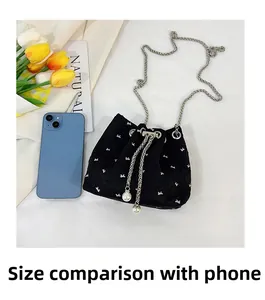Detail view of floral bucket bag with pearl drawstring beside a smartphone for scale