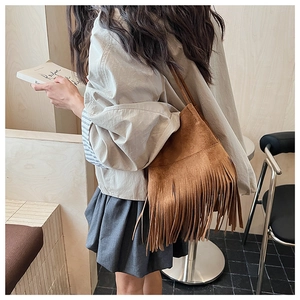 Detailed view of long tassels on a dark brown suede shoulder bag in a modern setting