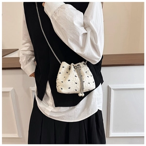 Detailed view of white bucket bag with black patterns, chain strap and pearl drawstrings