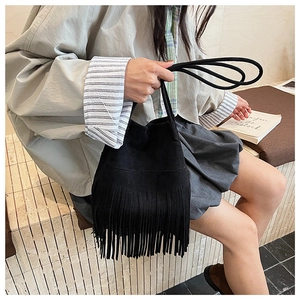 Close-up of bohemian black suede bucket bag featuring long dense fringe and shoulder strap