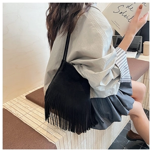 Detail shot of a black suede bucket bag with long fringe tassels shown on a model