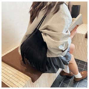 Detail of black fringe shoulder bag with matte texture on female model in casual setting