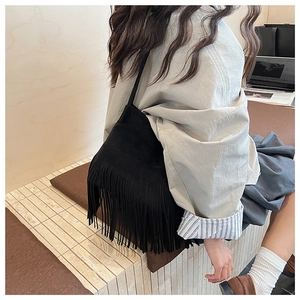 Detail shot of black suede shoulder bag featuring long flowing fringe and boho design