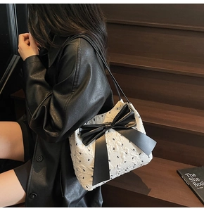Detail of white textured fabric shoulder bag with large black bow and slim strap