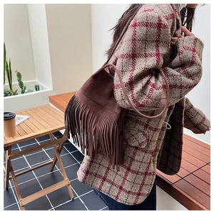Close-up of brown suede tassel bag styled with a plaid wool coat in autumn setting