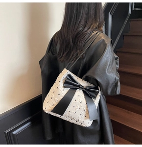 Detail of quilted tote bag with large black bow and small bow prints worn by a model