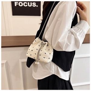 Detail of white quilted drawstring bucket bag with black bow patterns and pearl charms