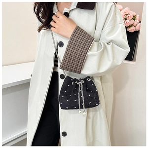 Detail of black drawstring bucket bag with bow print, silver chain, and pearl charms
