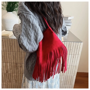 Close-up of a red fringe bucket bag styled with a knitted sweater and plaid skirt