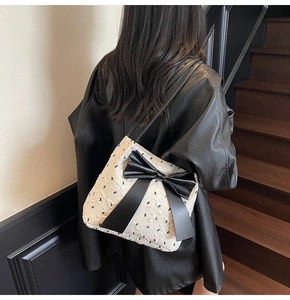 Model wearing ivory bow-patterned shoulder bag with large black decorative bow detail