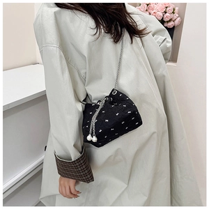 Detail of black pleated bucket bag with white bows, pearl drawstring, and metal chain strap