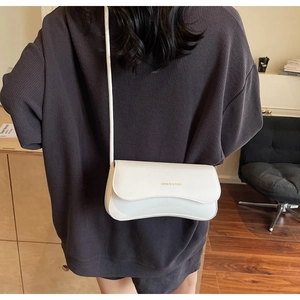 Close-up of a white minimalist shoulder bag with a unique wavy flap and gold lettering
