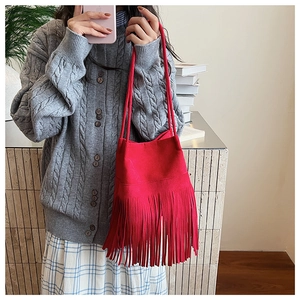 Close-up of vibrant red suede bucket bag with long tassels and delicate double handles