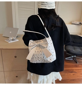 Close-up of a white pleated shoulder bag featuring a black bow and rabbit embroidery