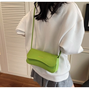 Detail of green rectangular flap bag with gold lettering shown on shoulder with long strap