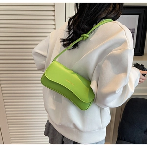 Detail of neon green baguette bag with knotted strap shown on model shoulder