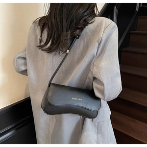 Close-up of black baguette shoulder bag worn with a gray suit in a street style setting