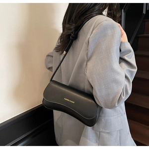 Detail of minimalist black baguette shoulder bag featuring gold lettering and sleek finish