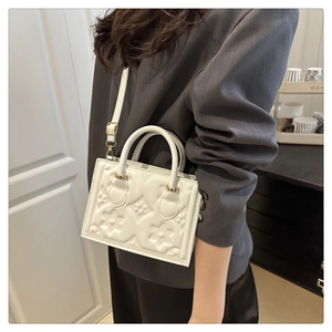 Detail view of white square handbag with floral embossing and adjustable shoulder strap