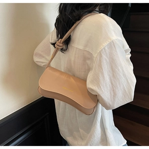 Detail of beige shoulder bag with knotted strap and gold print on a white linen shirt