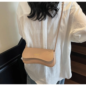 Detail of milk tea leather crossbody bag with wavy flap and gold text in lifestyle setting
