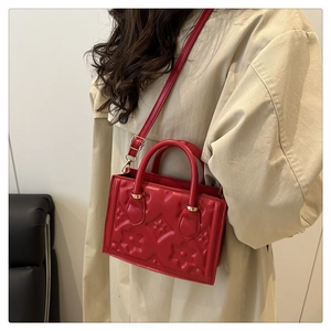 Detail of red embossed shoulder bag with floral pattern and gold metal hardware