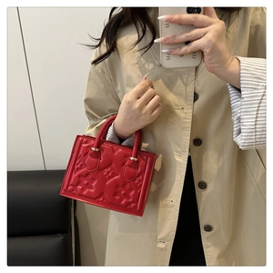 Close-up of red leather handbag featuring luxury floral embossed texture and gold hardware