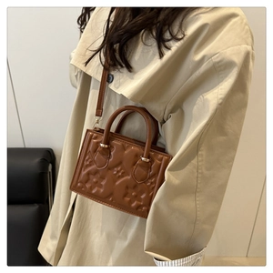 Caramel brown embossed floral leather handbag with gold hardware detail on a model