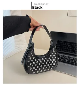 Dettaglio borsa a mezzaluna in pelle verniciata nera con borchie su tavolo bianco