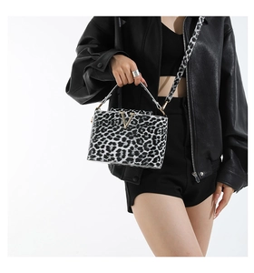 Detail of leopard print crossbody bag with gold V-buckle on black leather jacket