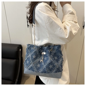 Detail of denim tote bag showing quilted star pattern and fringe trim with chain strap