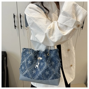 Detail of denim tote bag featuring white star prints, fringe edges, and gold chain strap