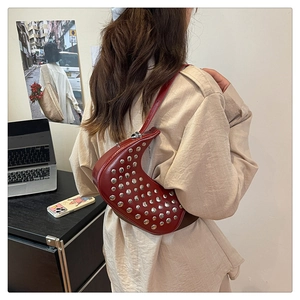 Dettaglio borsa a mezzaluna bordeaux con rivetti argentati indossata da una modella