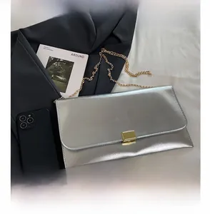 Détail d'une pochette enveloppe argentée avec texture cuir et fine chaîne dorée