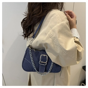 Dettaglio borsa a tracolla in denim blu con catena d'argento portata su trench-coat