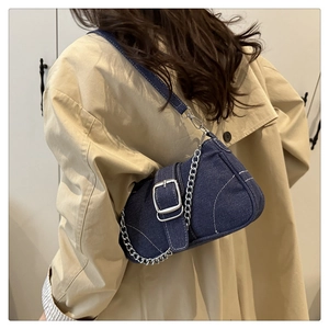 Blue denim crossbody bag featuring a silver chain detail worn by a model in a trench coat