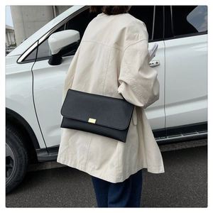 Gros plan du sac enveloppe en cuir saffiano noir avec boucle dorée et bandoulière chaîne