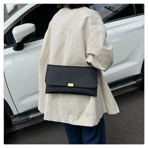 Close-up of black leather square bag with gold buckle and chain strap by a white car