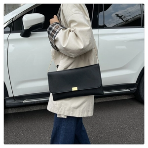 Détail d'un sac bandoulière en cuir grainé noir avec boucle dorée rectangulaire et chaîne