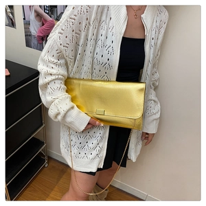 Detail of a metallic gold envelope clutch with chain strap on a stylish model outfit