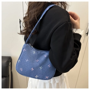 Detail shot of blue denim shoulder bag featuring colorful bow embroidery and zipper