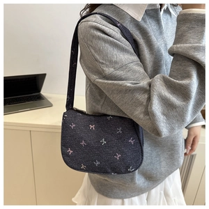 Detail of denim blue shoulder bag featuring pink and light green bow embroidery patterns